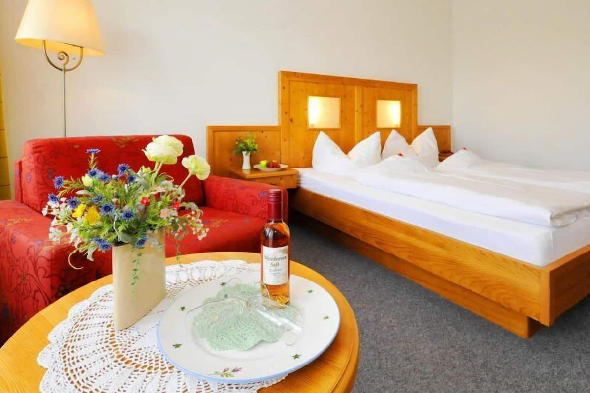 Et hotelværelse med en træseng, en rød sofa, et lille bord med en vase blomster og en flaske vin.