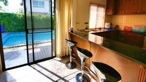 Una cocina con puerta de cristal que da a una piscina, armarios de madera y una zona de bar con taburetes.