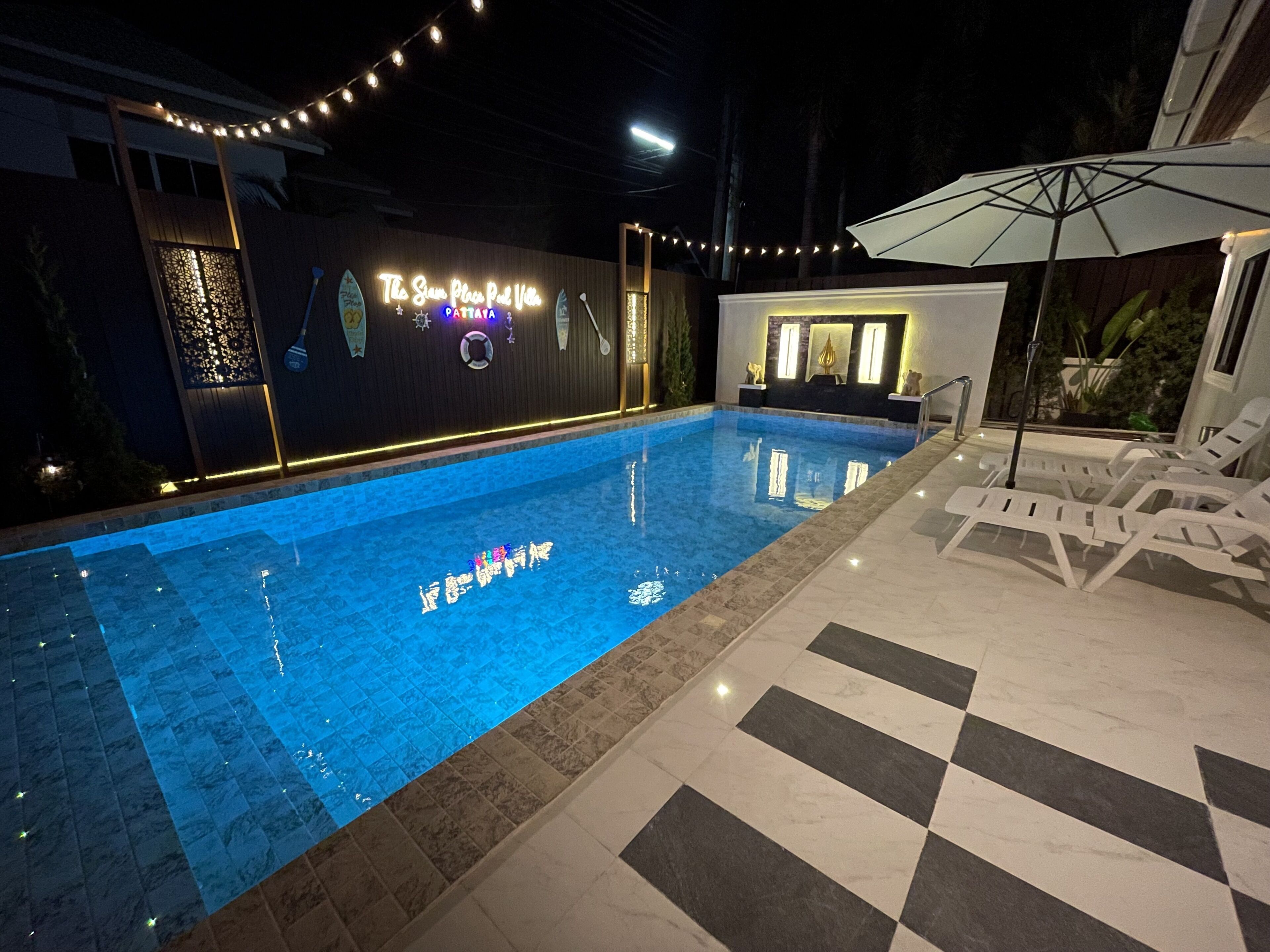 Une piscine dont le fond est recouvert de carreaux, avec des chaises longues et des guirlandes lumineuses.