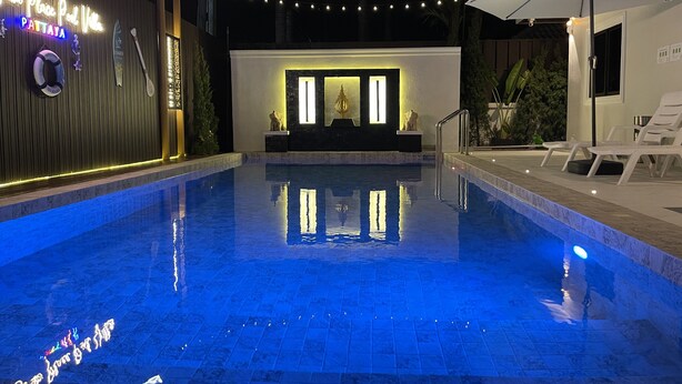 Una piscina con piso de azulejos y una pequeña cascada. Hay sillones de descanso y una sombrilla a la derecha.