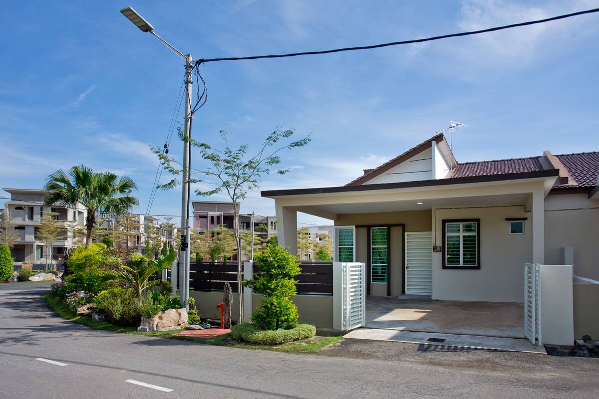 A residential building with a covered porch, a street lamp, and a small garden with various plants and a palm tree.