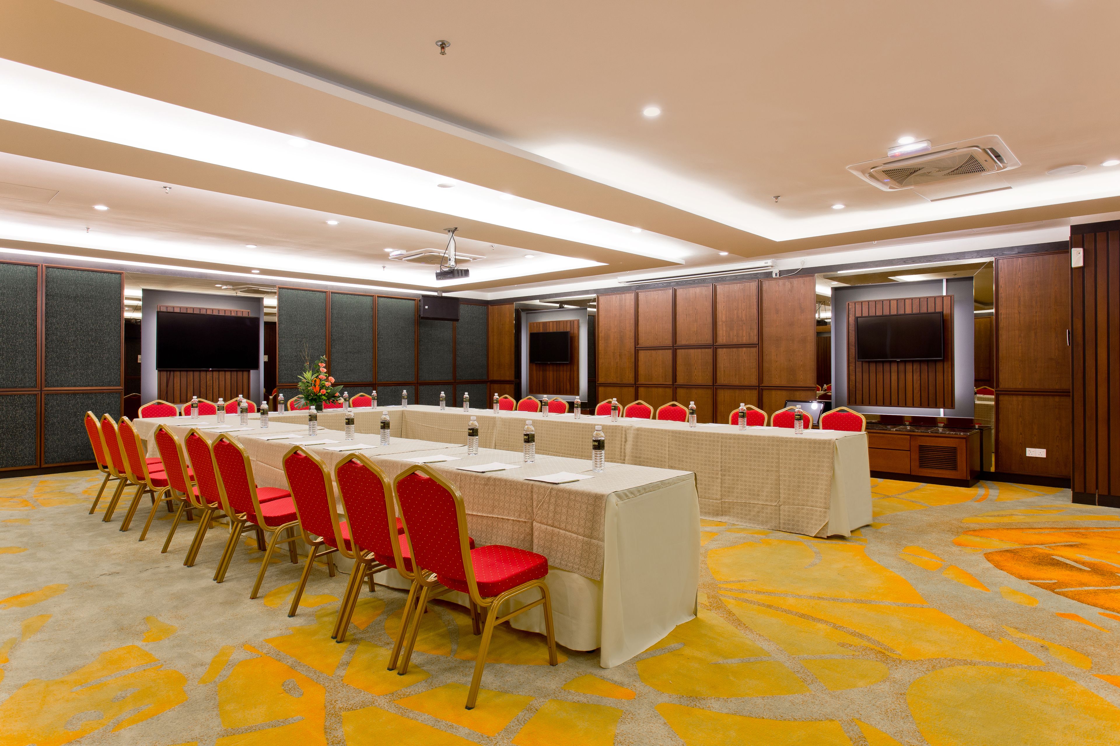 A conference room with a long table, red chairs, and a television screen.