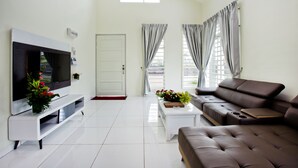 A modern living room with a flat-screen TV, a sofa, a coffee table, and a TV stand. - MBI Desaku Homestay (Karangan)