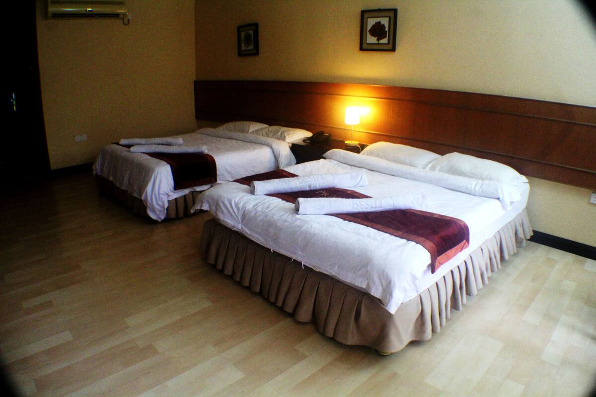 A hotel room with two single beds, a wooden headboard, a nightstand with a lamp, and a framed picture on the wall.