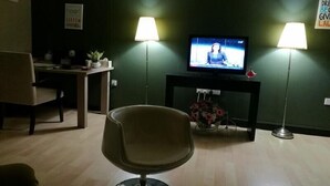 Una sala de estar con televisión, dos lámparas, una silla, un escritorio y una planta en maceta.