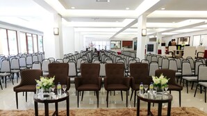 Una amplia sala de conferencias con filas de sillas y mesas, algunas con centros de mesa florales.
