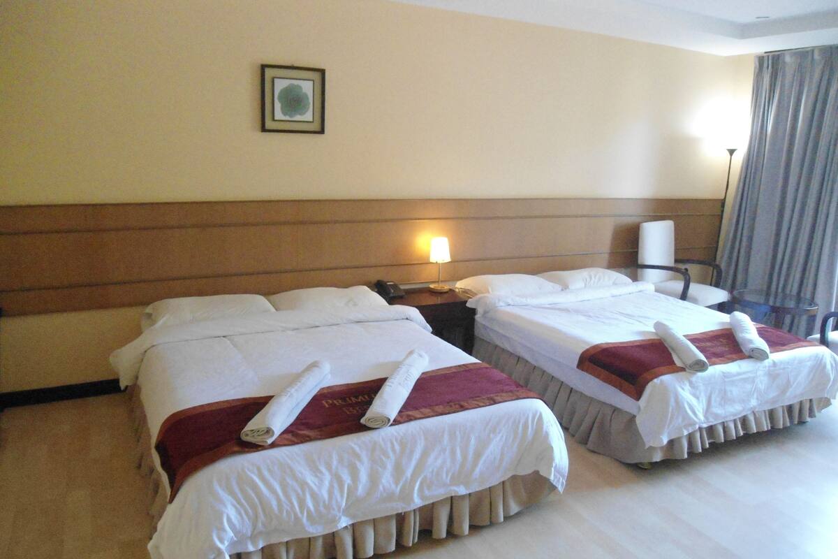 A hotel room with two beds, a nightstand with a lamp, a chair, and a framed picture on the wall.