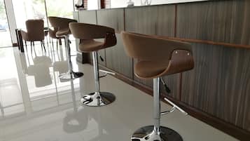 A row of modern bar stools with chrome bases and cushioned seats, positioned in a well-lit room with a large window and decorative items on the wall.