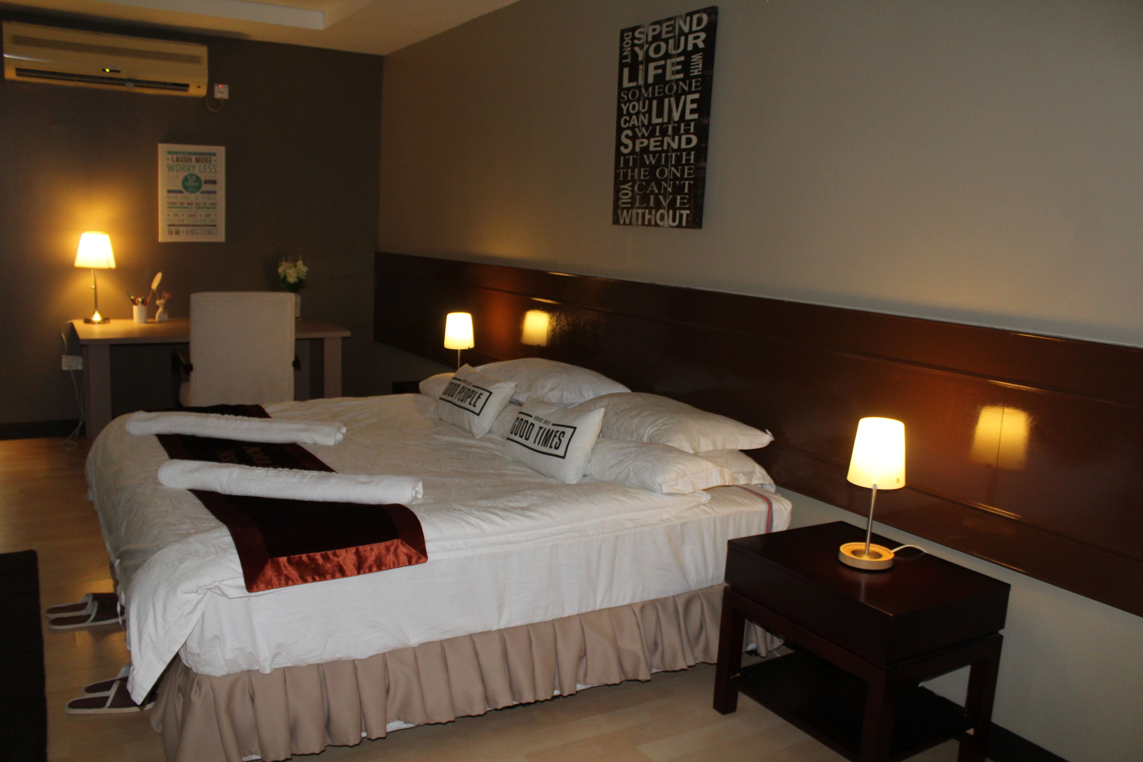 A neatly made bed with pillows, a bedside table with a lamp, and a wall sign.