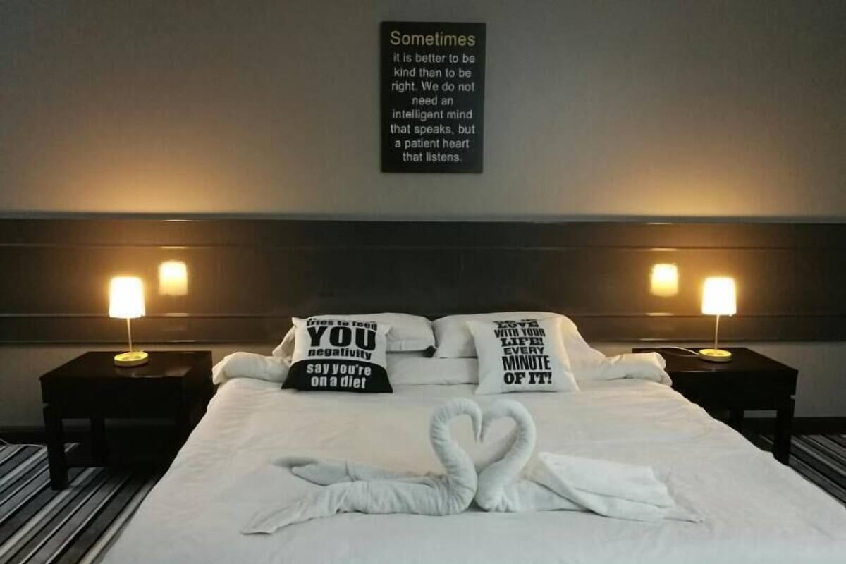 A hotel room with a neatly made bed, two bedside lamps, and motivational pillows.