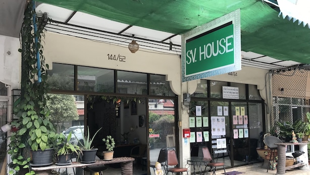 A storefront with a green awning, a sign reading "SV. HOUSE", and various potted plants outside.