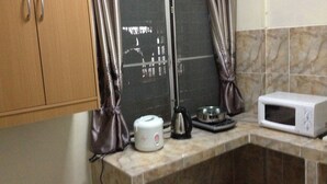 Una cocina con microondas, hervidor y una ventana con cortinas.