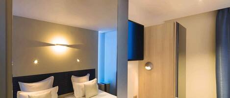 A modern hotel room with two beds, a flat-screen TV mounted on the wall, and a shower area.