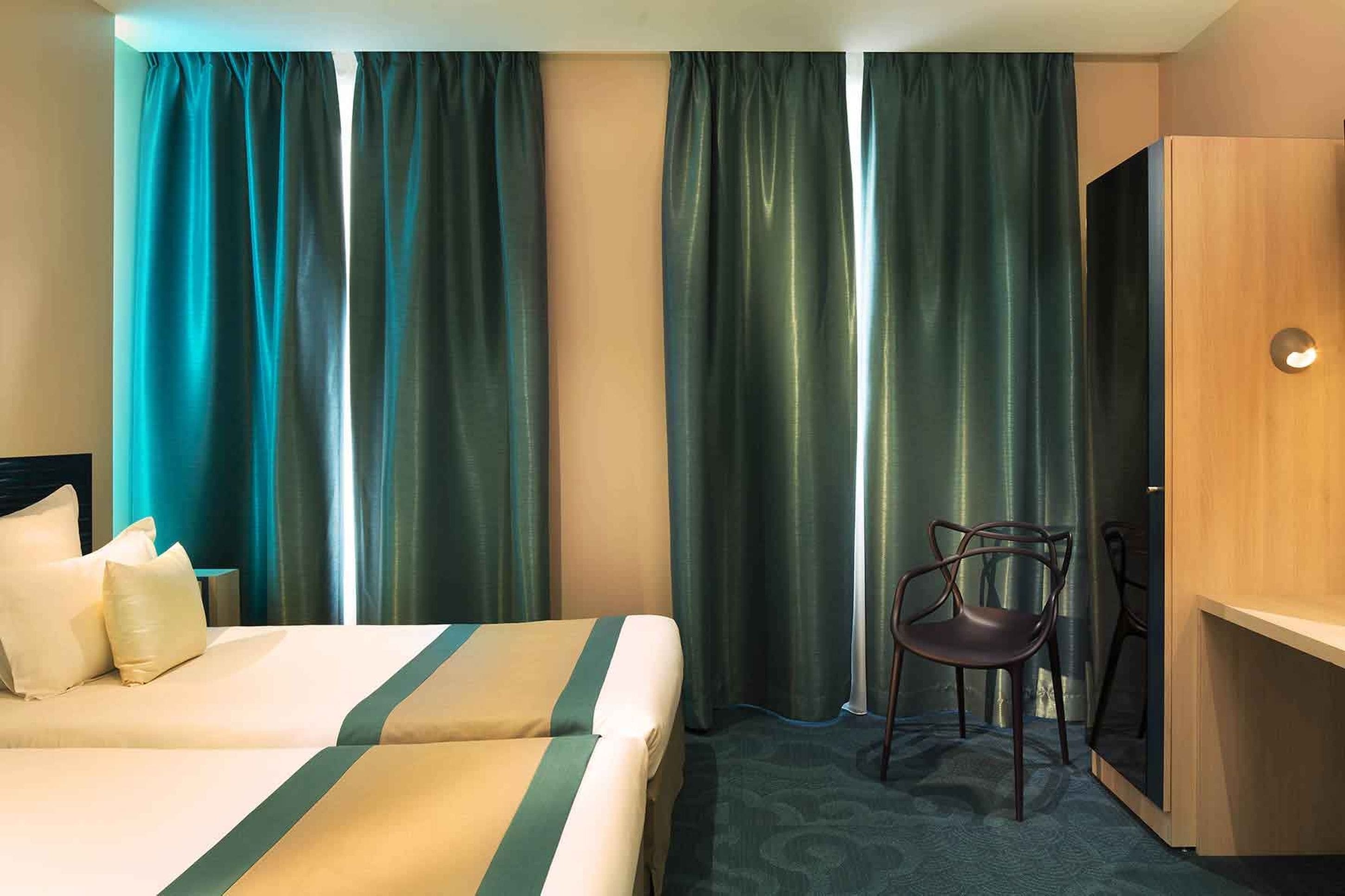 A hotel room with a bed, a chair, and curtains.