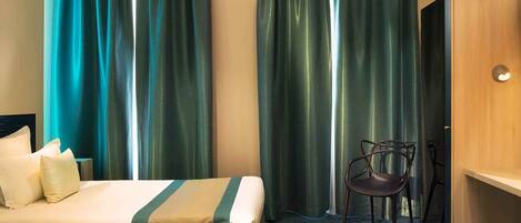 A hotel room with a bed, a chair, and curtains.