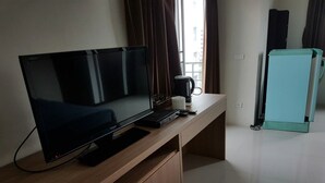 A modern hotel room with a large flat-screen TV on a wooden desk, a coffee maker, and a small refrigerator. - CM House (Bangkok)