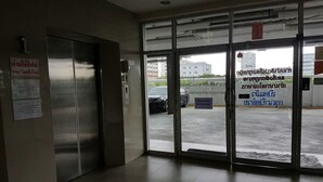 A hotel entrance with a glass door, a sign in a foreign language, and a car parked outside. - CM House (Bangkok)