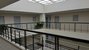 A multi-level interior with a central open space, glass railings, and doors labeled with numbers. - CM House (Bangkok)