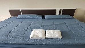 A neatly made bed with a blue bedspread, two pillows, and two folded white towels. - CM House (Bangkok)
