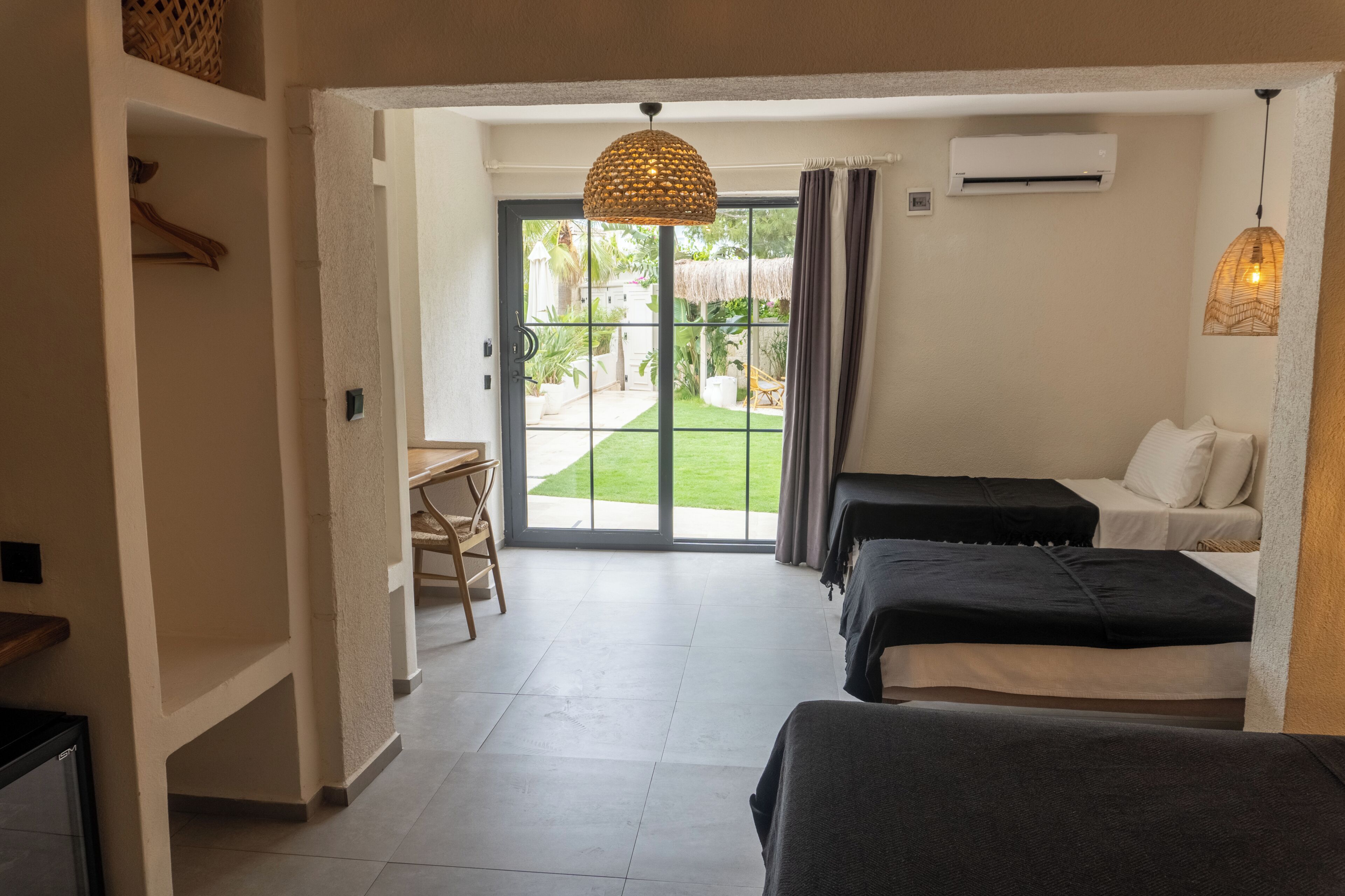 Een hotelkamer met een bed, een bureau en uitzicht op een tuin door een glazen deur.