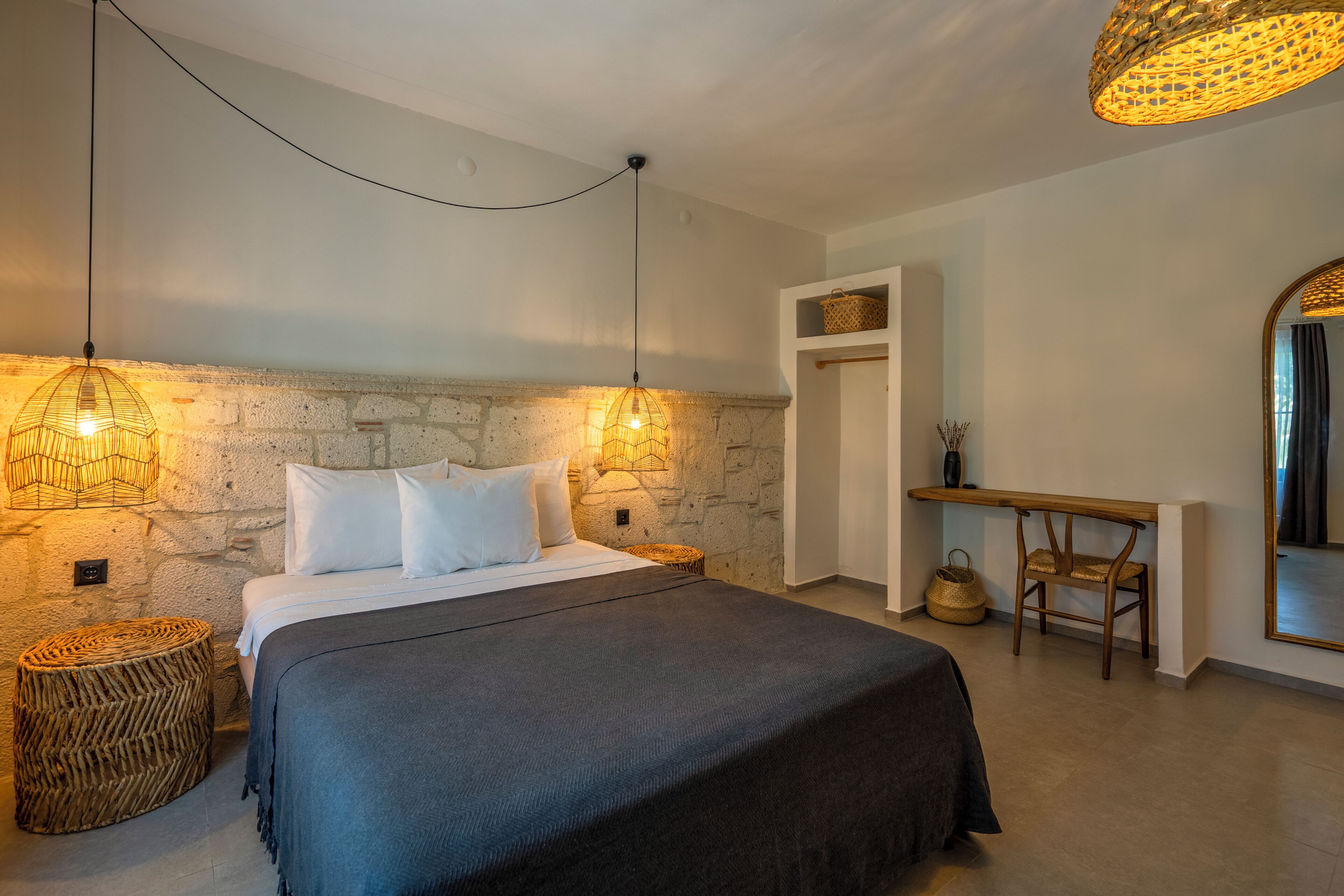 Une chambre avec un mur en pierre, un lit avec une literie blanche, un bureau en bois et une chaise en osier.