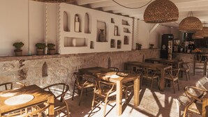 Un interior rústico con mesas y sillas de madera, una pared de piedra y lámparas colgantes de fibras.