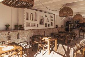 Un interior rústico con mesas y sillas de madera, una pared de piedra y lámparas colgantes de fibras.