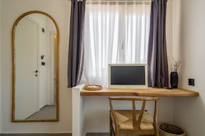A room with a wooden desk, a laptop, a chair, a mirror, and a window with curtains.