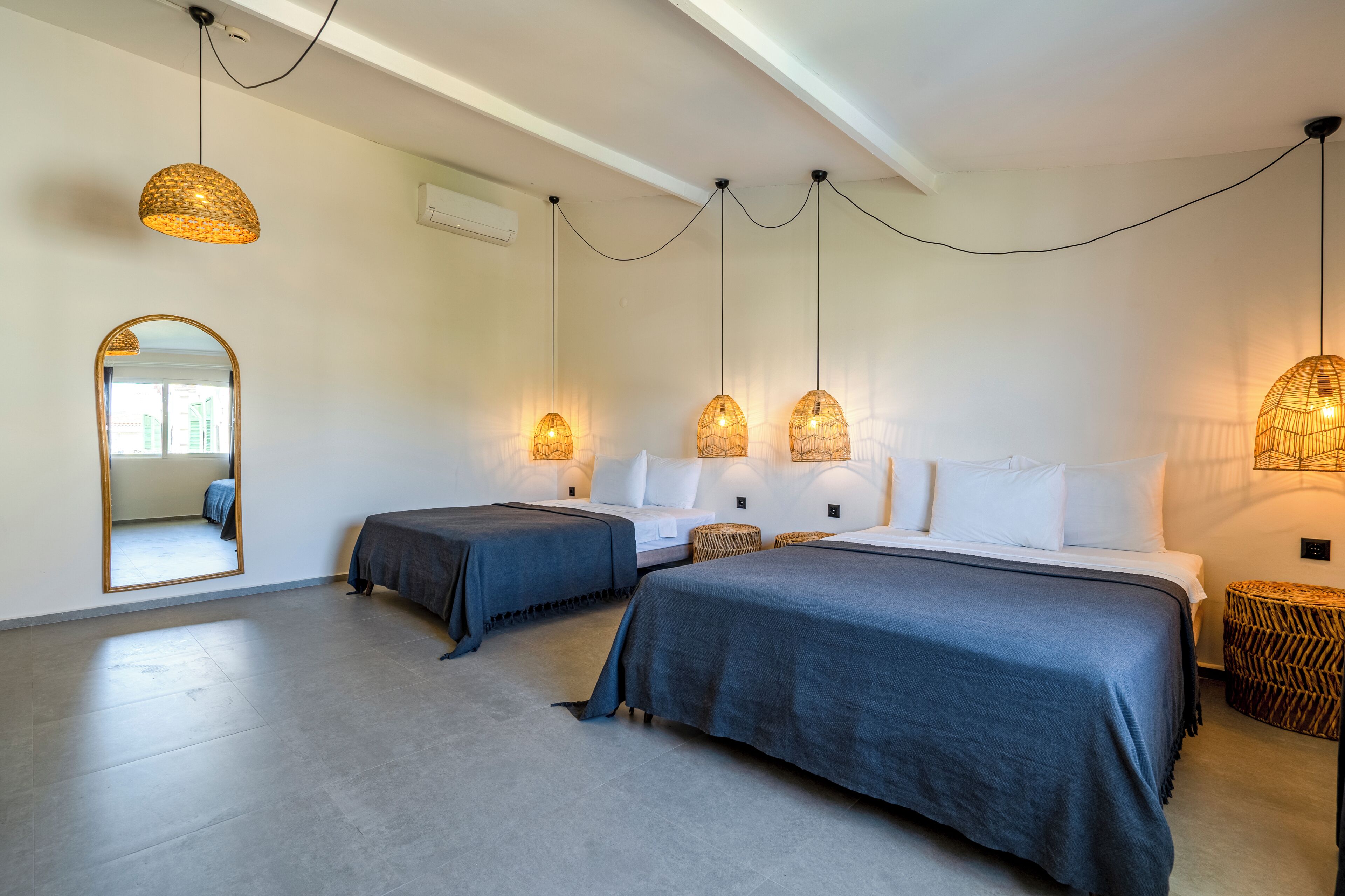 A hotel room with two beds, a large mirror, and hanging pendant lights.