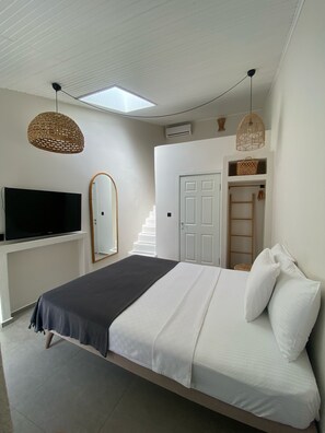 Quarto com uma cama, televisão, espelho, escada e porta.