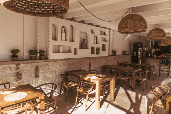 Un interior rústico con mesas y sillas de madera, una pared de piedra y lámparas colgantes de fibras.