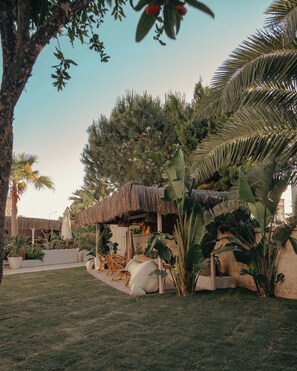 A tropical garden with a thatched-roof structure, potted plants, and outdoor seating. - Art Alacati (Cesme)