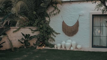 A garden with a white wall, large white vases, and a hanging woven basket.