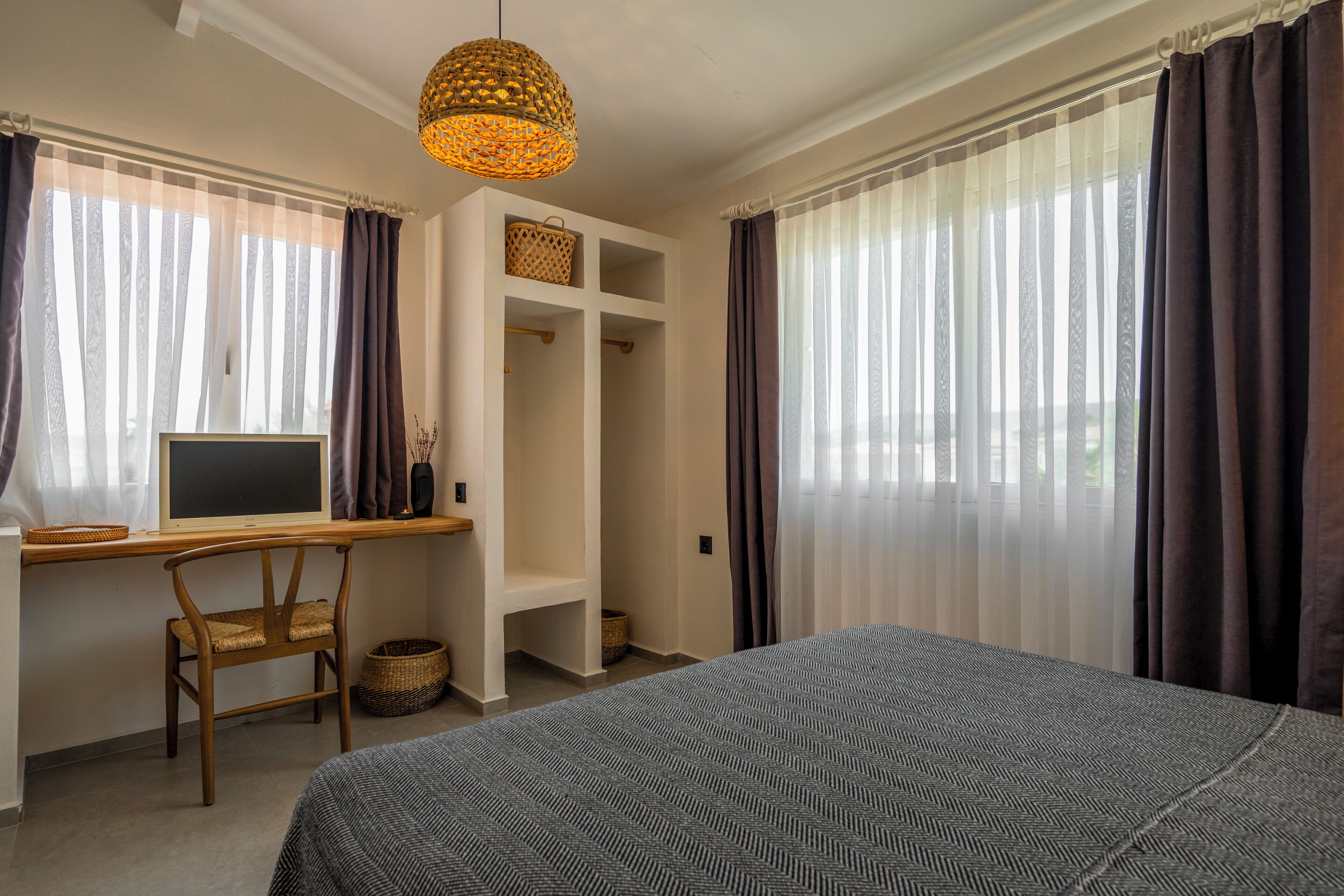 A bedroom with a bed, a desk with a computer, a chair, and a hanging light fixture.