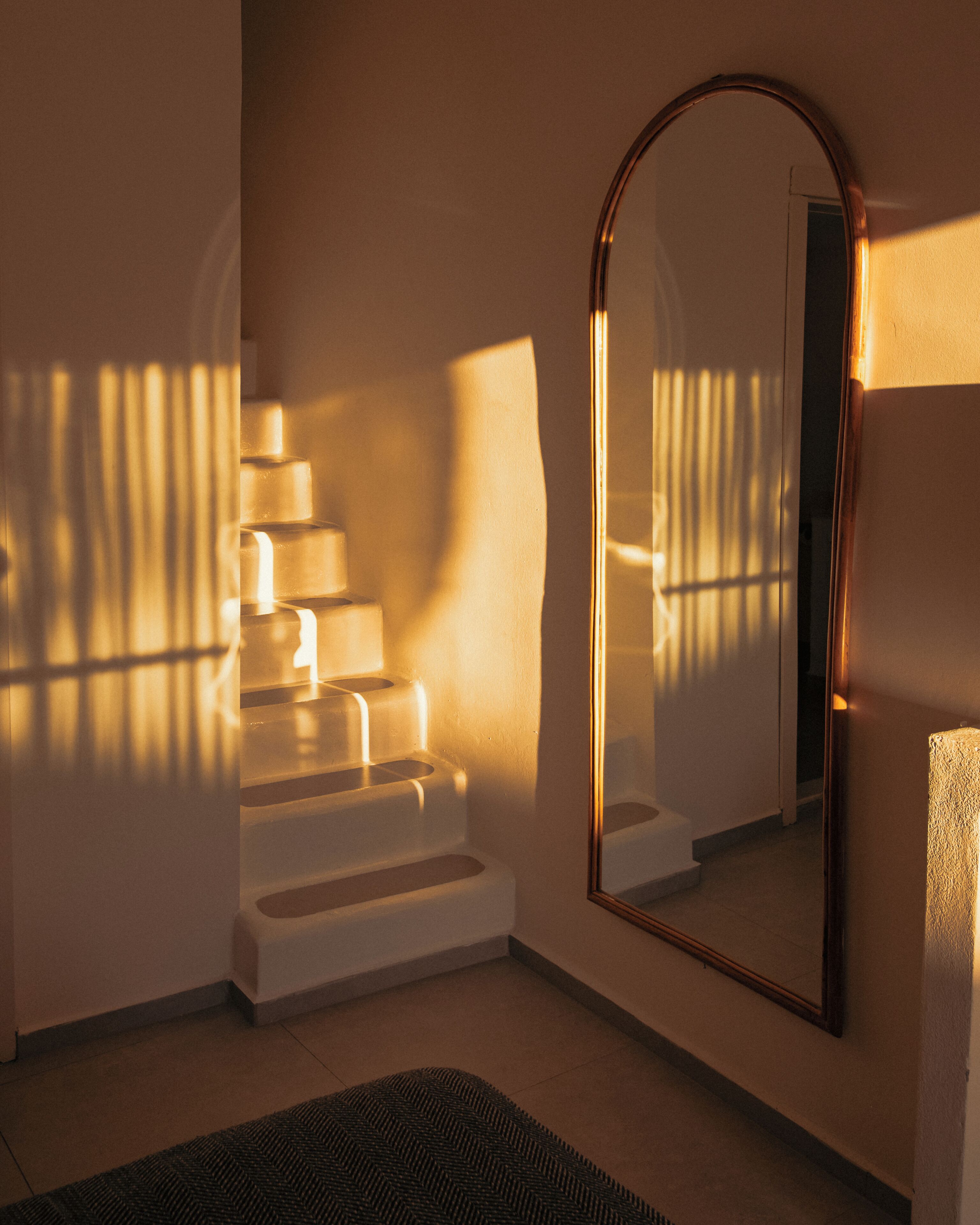 Eine Treppe mit einem Spiegel, der den Raum reflektiert, einem Teppich auf dem Boden und einer Wand mit einer Lichtquelle, die Schatten wirft.