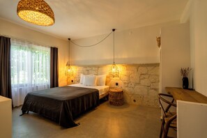 A bedroom with a bed, two wall-mounted lights, a stone wall, a small round table, and a chair. - Art Alacati (Cesme)