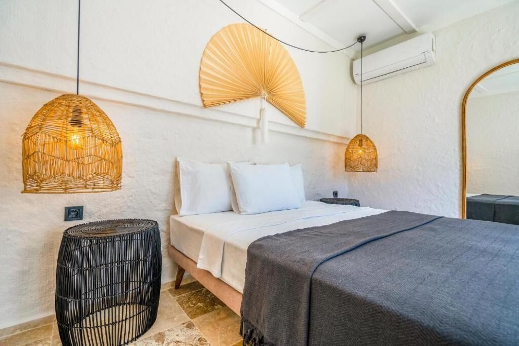 Une chambre à coucher avec un lit, des tables de chevet, un ventilateur suspendu et un tabouret rond en osier.