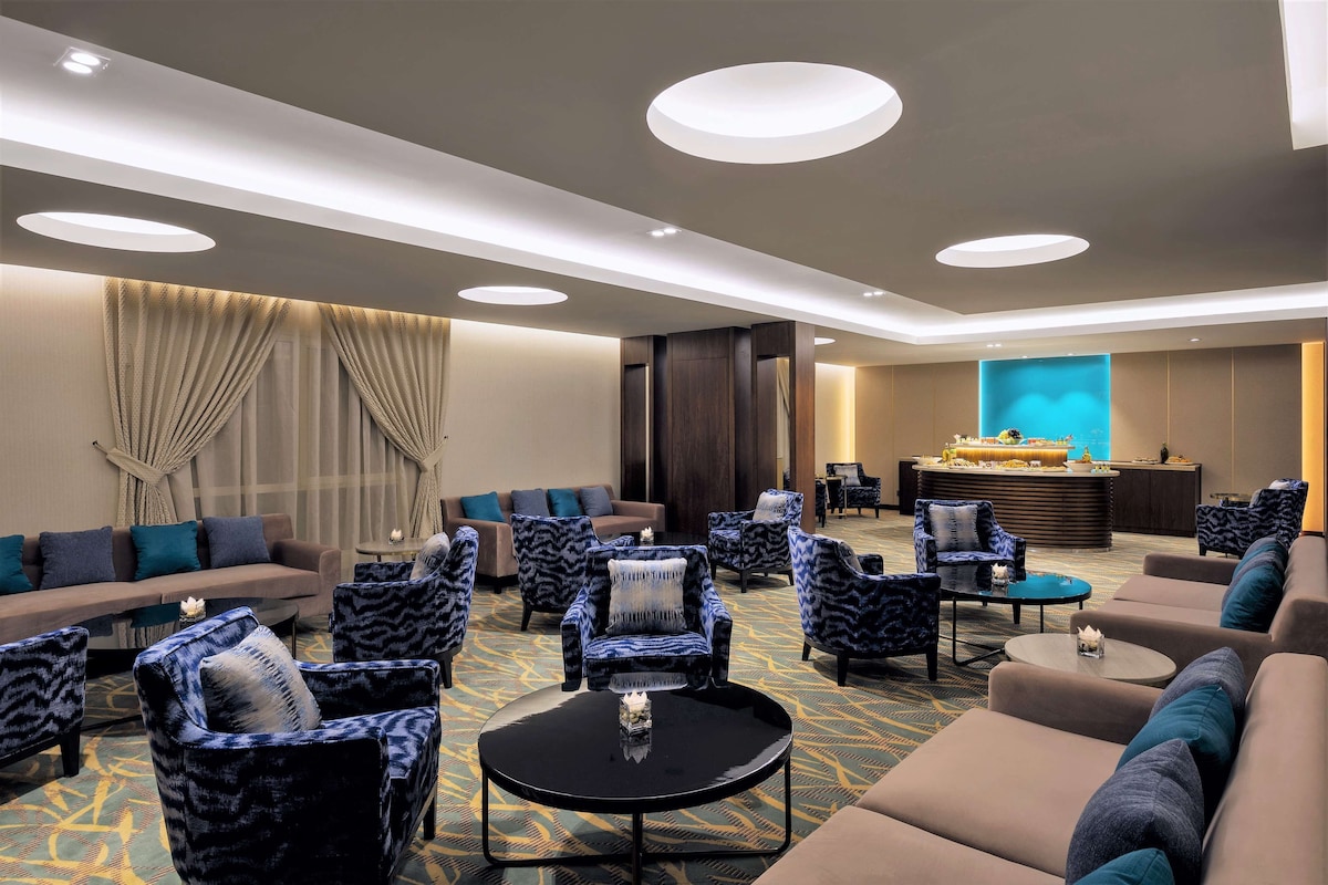 A hotel lobby with sofas, armchairs, a reception desk, and a patterned carpet.