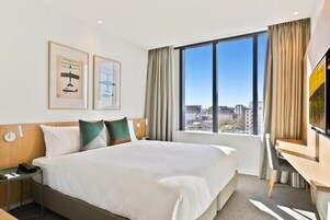 Habitación de hotel con una cama grande, un escritorio y vistas a la ciudad por la ventana.