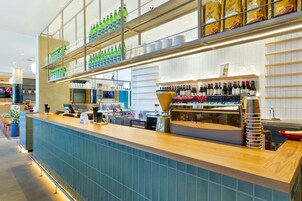 Zona bar moderna con un lungo bancone, scaffali pieni di bottiglie d'acqua e una selezione di bottiglie di vino.