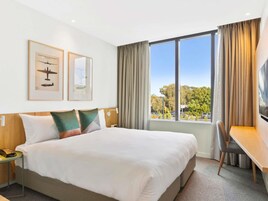 Habitación de hotel con una cama grande, un escritorio y vistas a árboles y edificios.