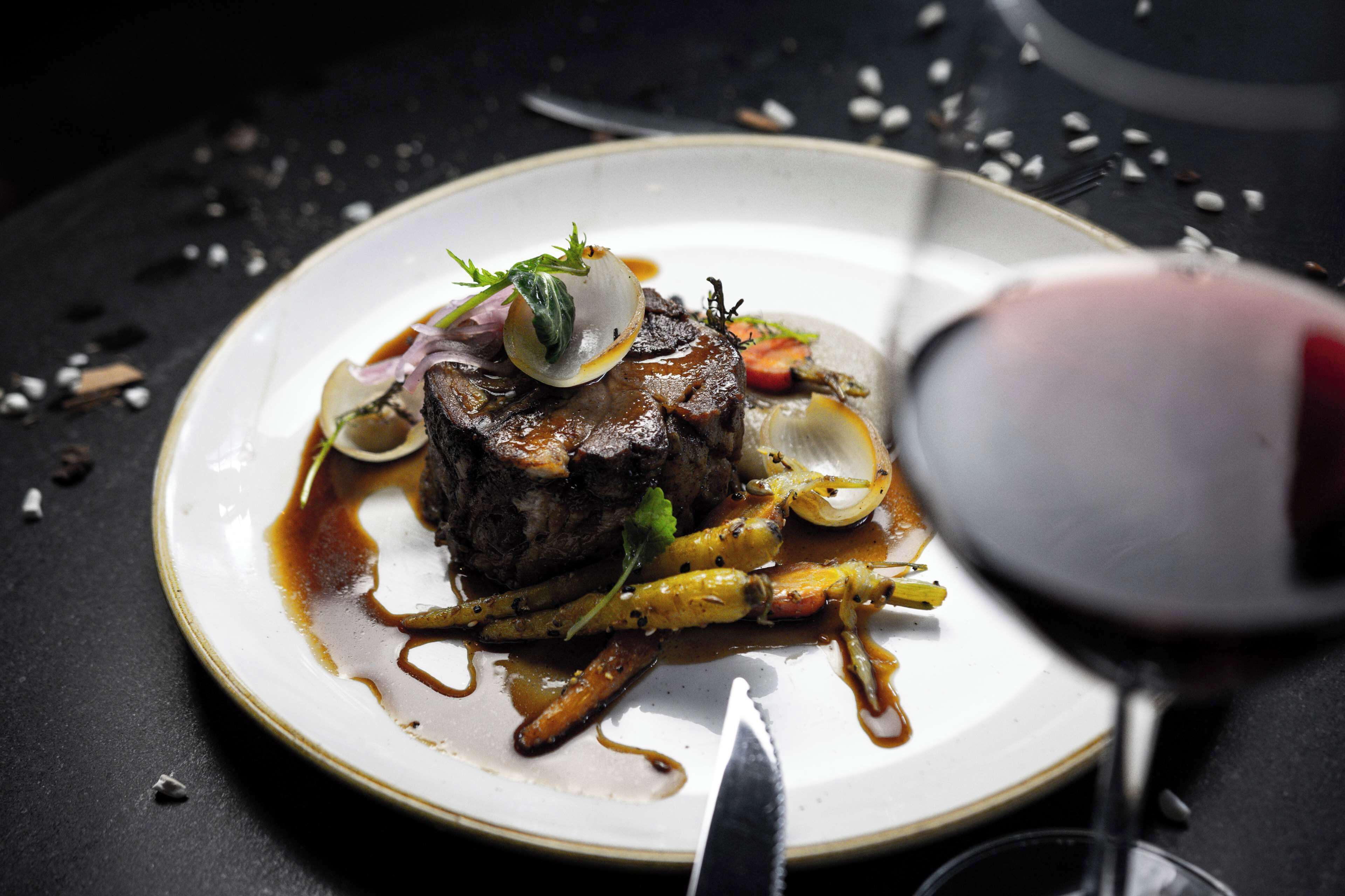 Un plato de comida con un cuchillo y una copa de vino tinto sobre una superficie oscura.