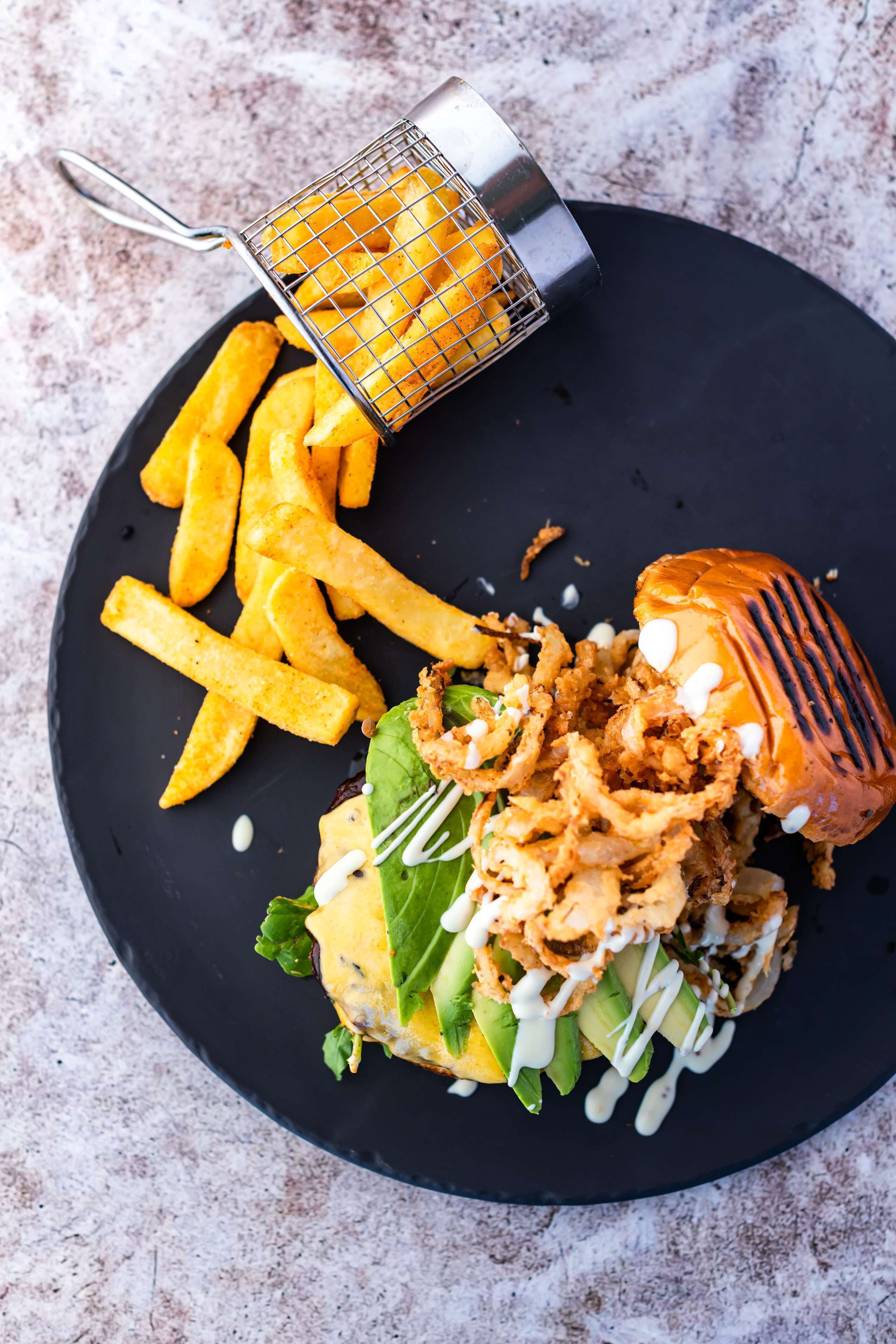 A plate with a burger, fries, and a grilled item, possibly a chicken wing, on a dark plate.