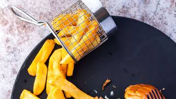 En tallrik med en hamburgare, pommes frites och något grillat, eventuellt en kycklingvinge, på en mörk tallrik.