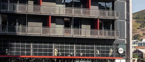 Un edificio de varios pisos con balcones, un toldo rojo y señalización que indica un restaurante.