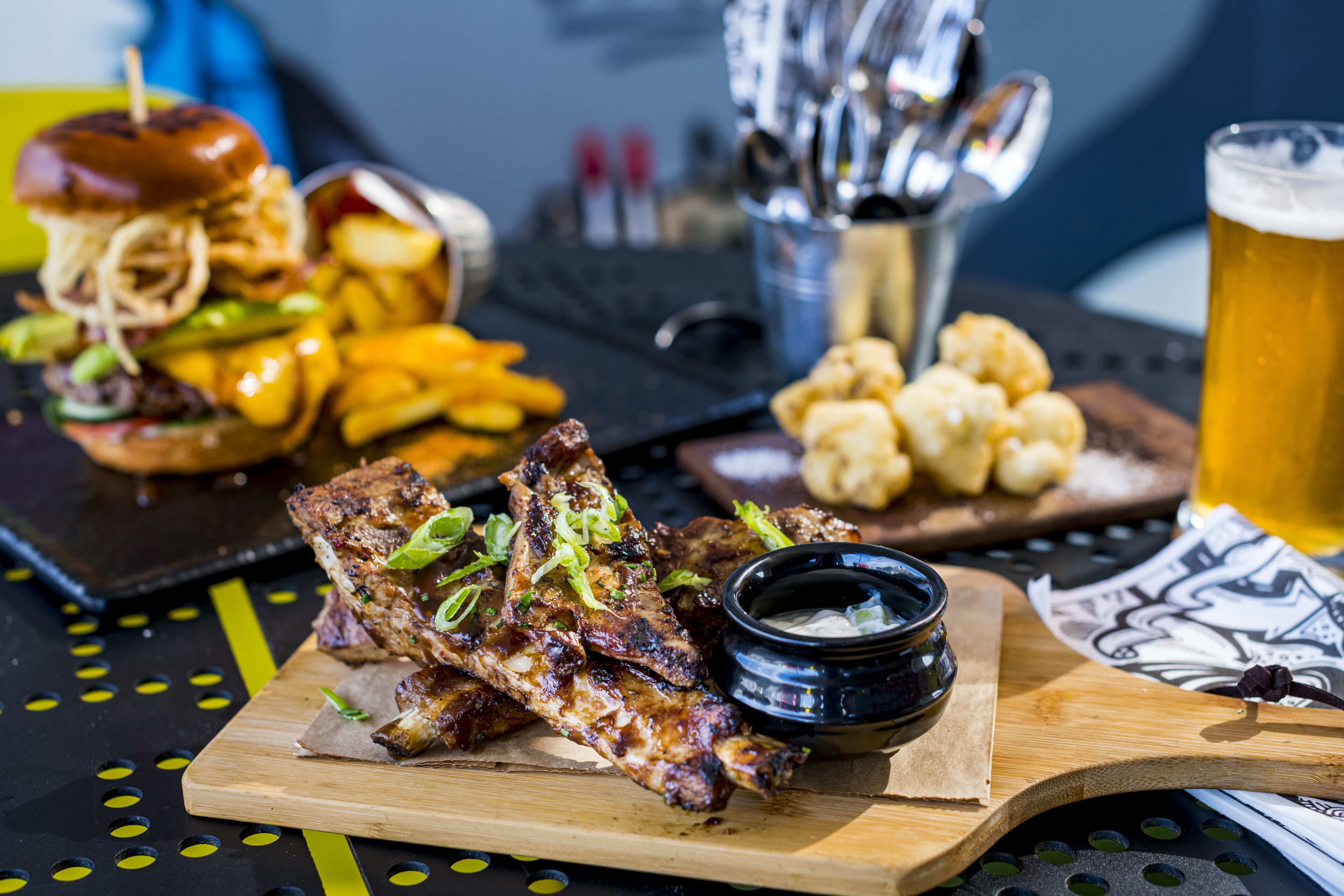 A meal with ribs, fries, a burger, and a beer on a table.