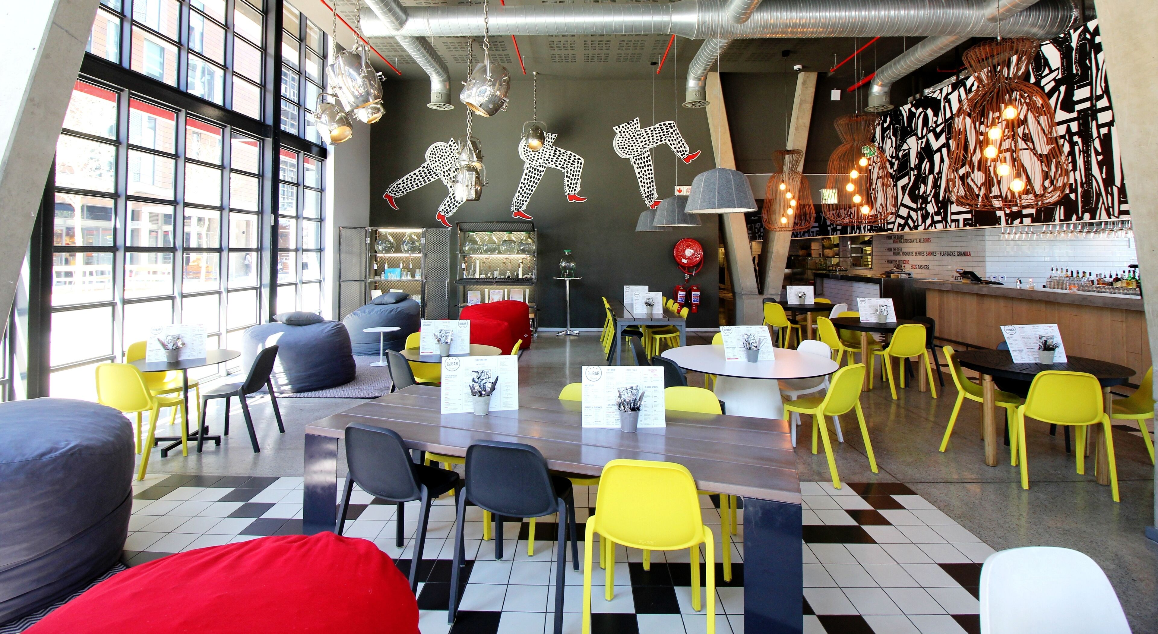 Un café moderno con diferentes opciones de asientos, incluyendo mesas, sillas y una barra, con luces decorativas colgantes.