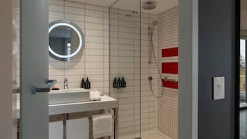 A modern bathroom with a glass shower enclosure, a white sink with a mirror, and red-tiled walls.