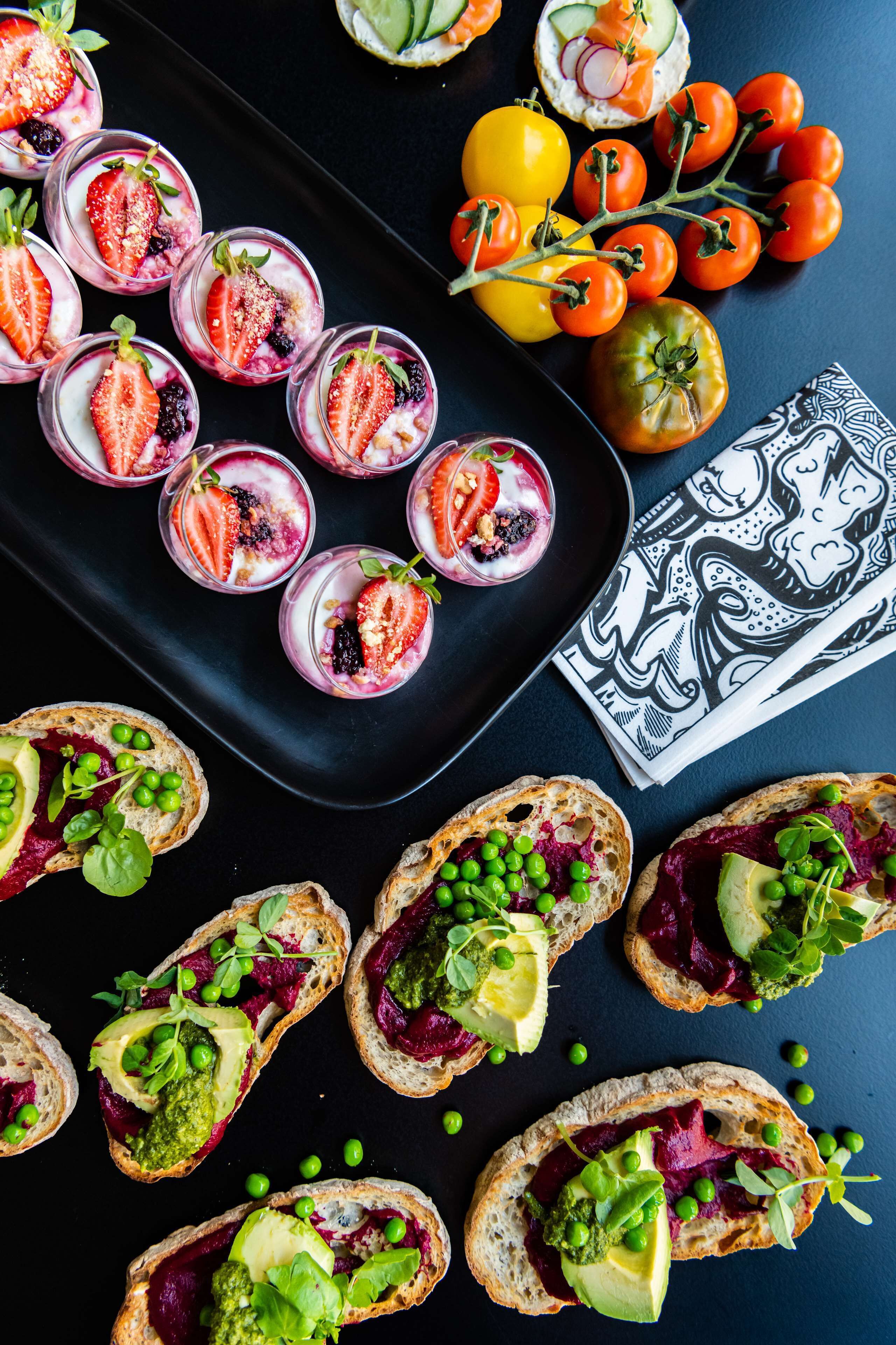 Diversos aperitivos, entre ellos bowls de fruta y pan con salsas, sobre una superficie oscura con una servilleta blanco y negro.
