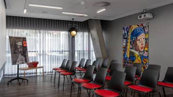 A conference room with rows of black chairs with red cushions, a projector on the ceiling, a poster on the wall, and a banner on a stand.